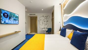A hotel room with a bed, a TV on the wall, a desk, and a chair.