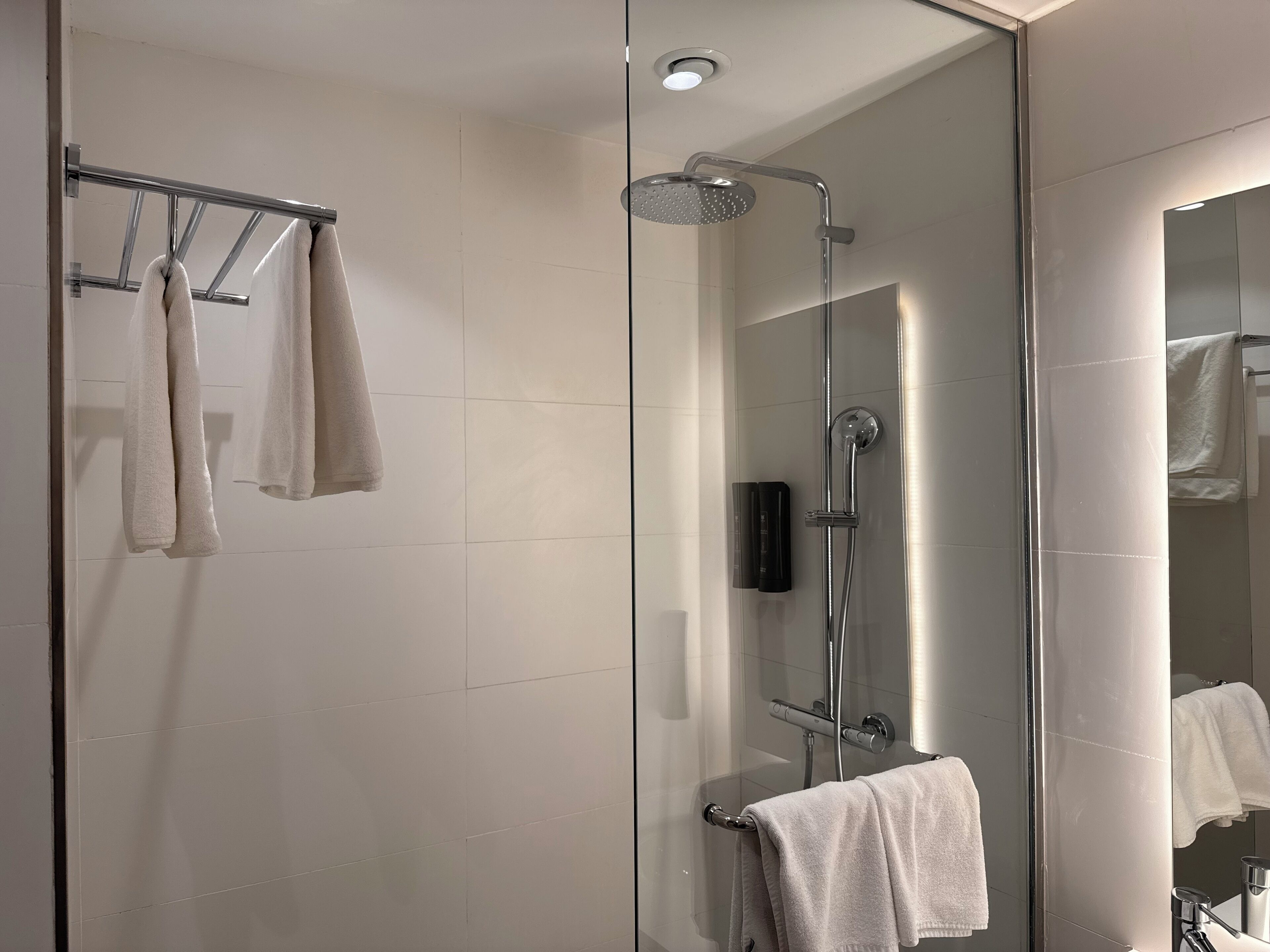 Um banheiro moderno com box de vidro, porta-toalhas com várias toalhas e um espelho refletindo o banheiro.
