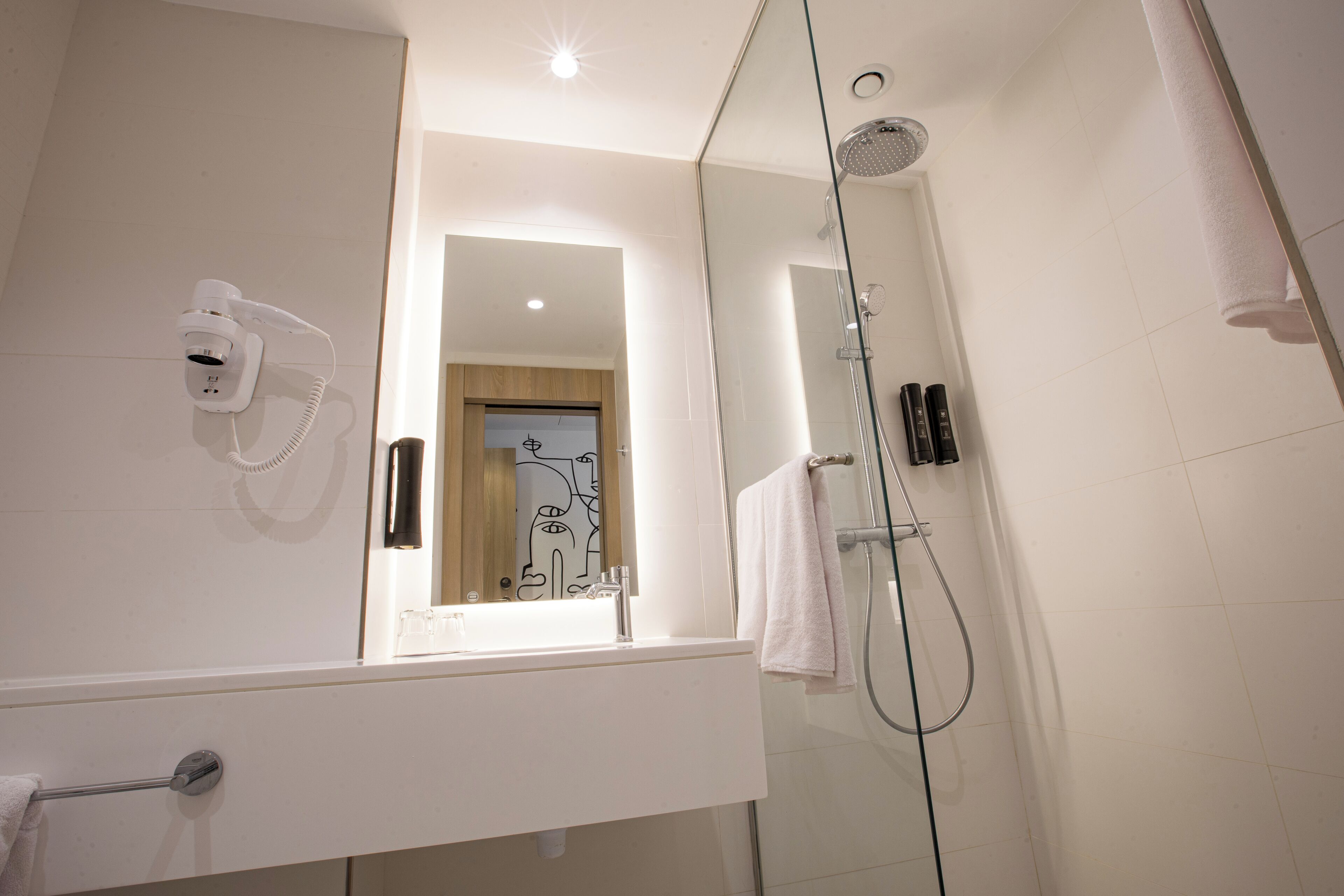 A modern bathroom with a glass shower enclosure, a hairdryer mounted on the wall, and a visible towel rack.