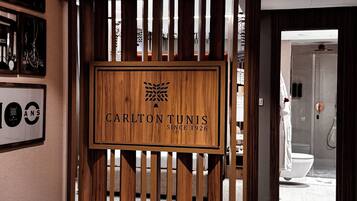 Un espace d’accueil agrémenté d’une cloison en bois sur laquelle est inscrit le nom « Carlton Tunis » et d’un panneau encadré indiquant « 100 ans ».