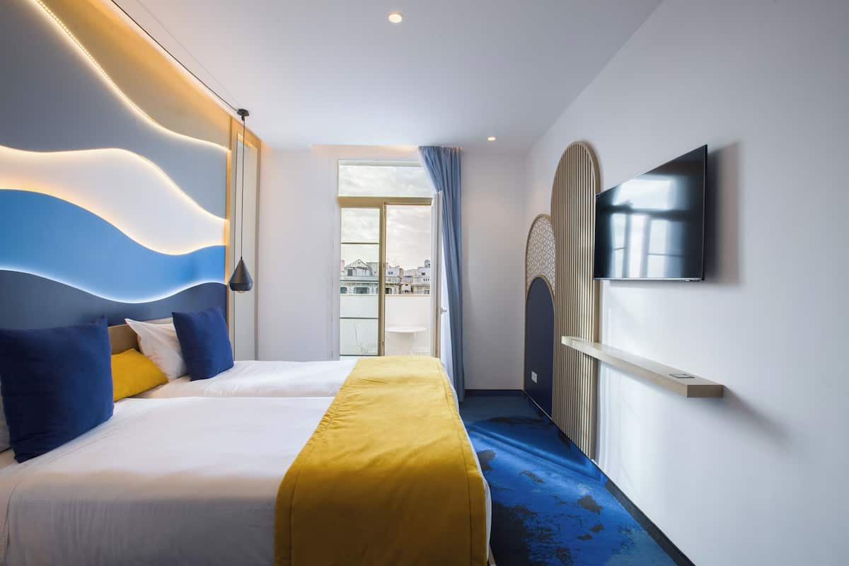 A hotel room with a bed, a TV, a window, and a view of the city.