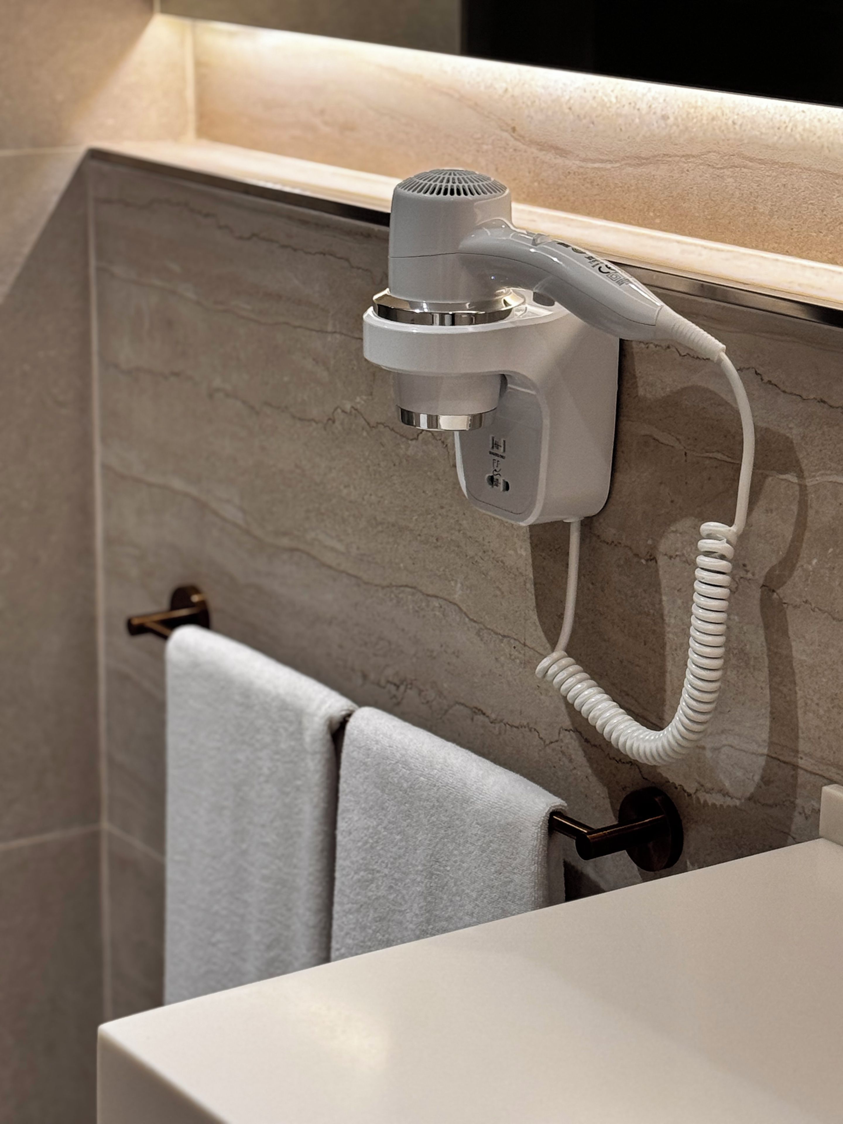 A hair dryer mounted on a wall in a bathroom with a towel rack and a sink.
