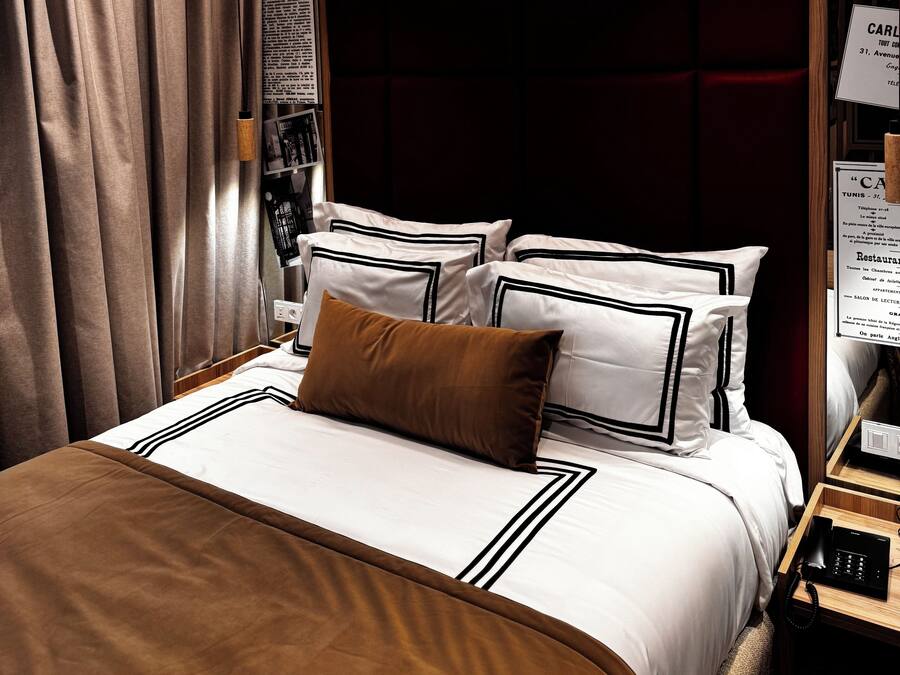 Habitación de hotel con cama, mesita de noche, teléfono y un cartel que dice 'Carlton Tunis Desde 1926'.