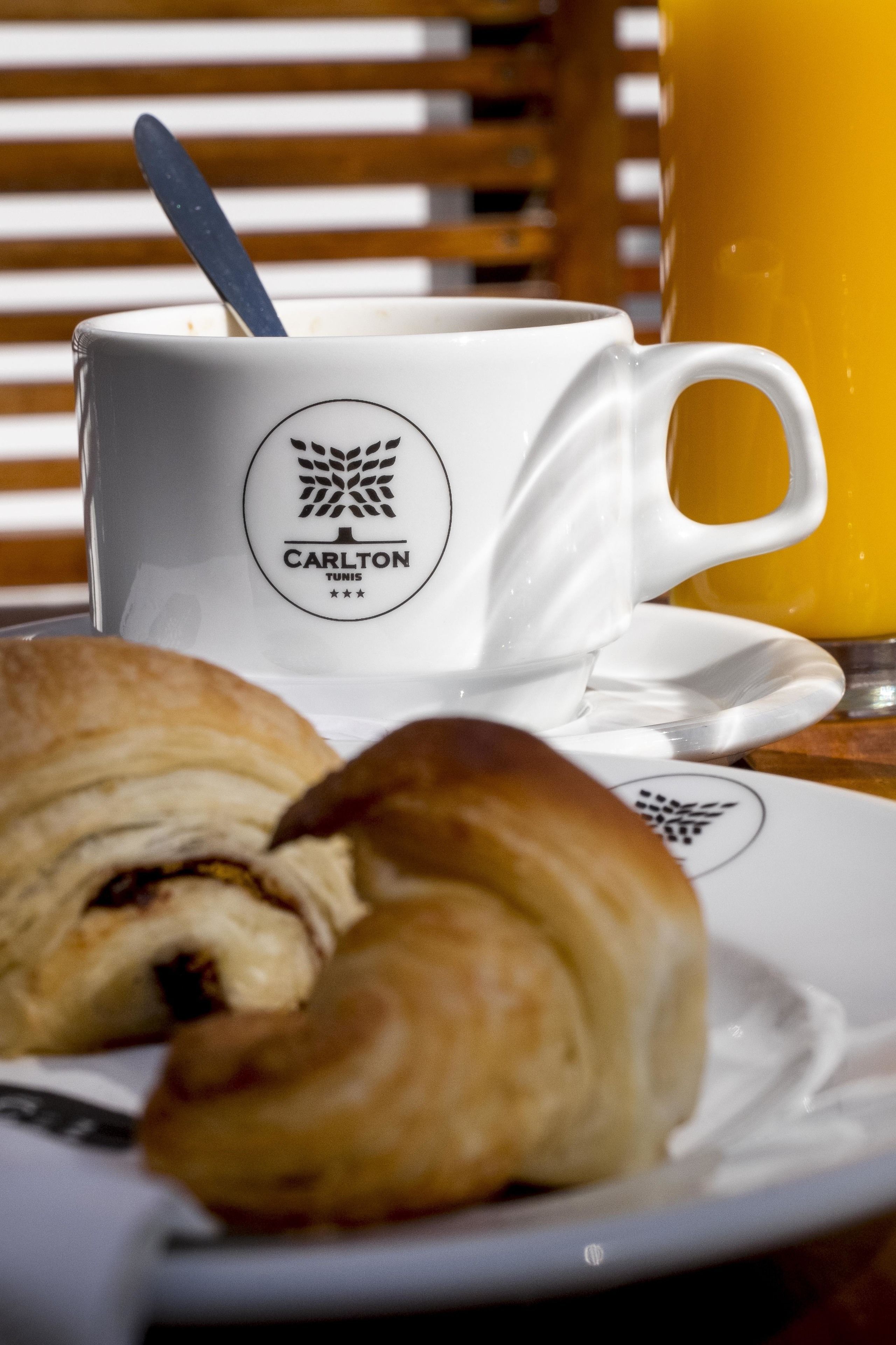 Een witte koffiekop met lepel, een croissant en een glas sinaasappelsap op een tafel.