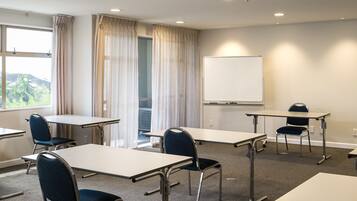 Sala de conferência com mesas, cadeiras, quadro branco e janela com cortinas.