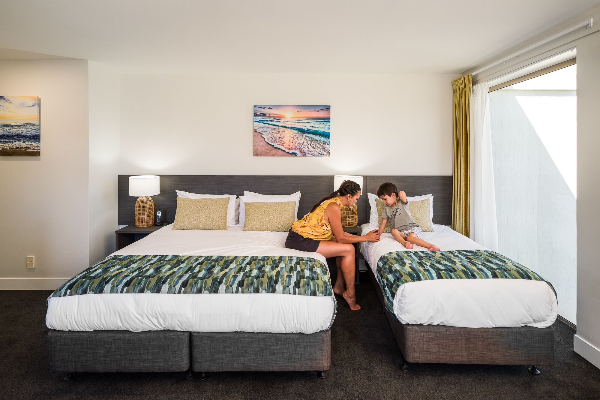 Una habitación de hotel con dos camas, una mesita de noche con lámpara y un cuadro en la pared.