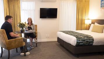 A hotel room with a bed, a TV, a table with chairs, and a window with curtains.
