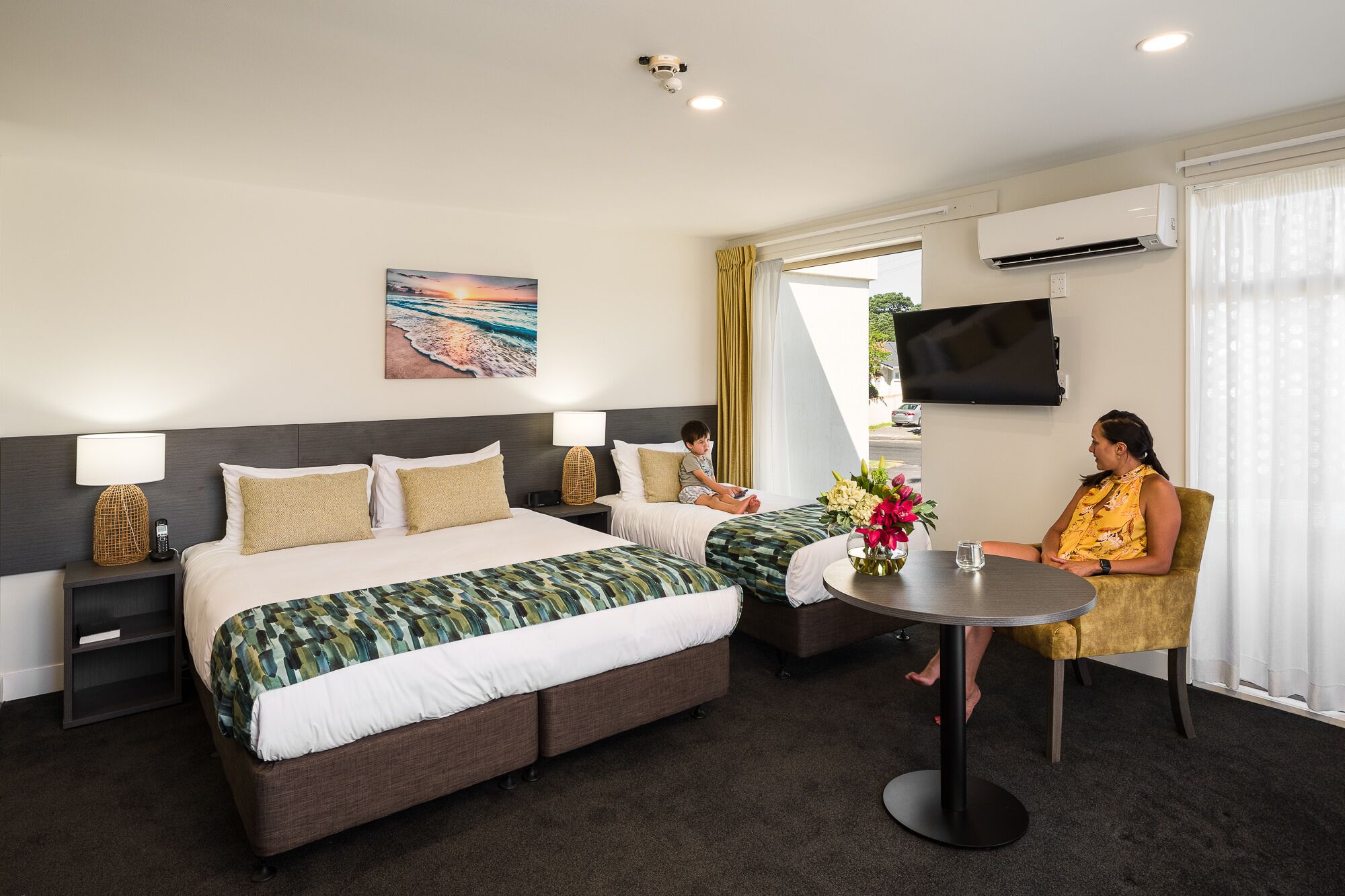 A hotel room with a bed, a sofa, a TV, and a table with a vase of flowers.