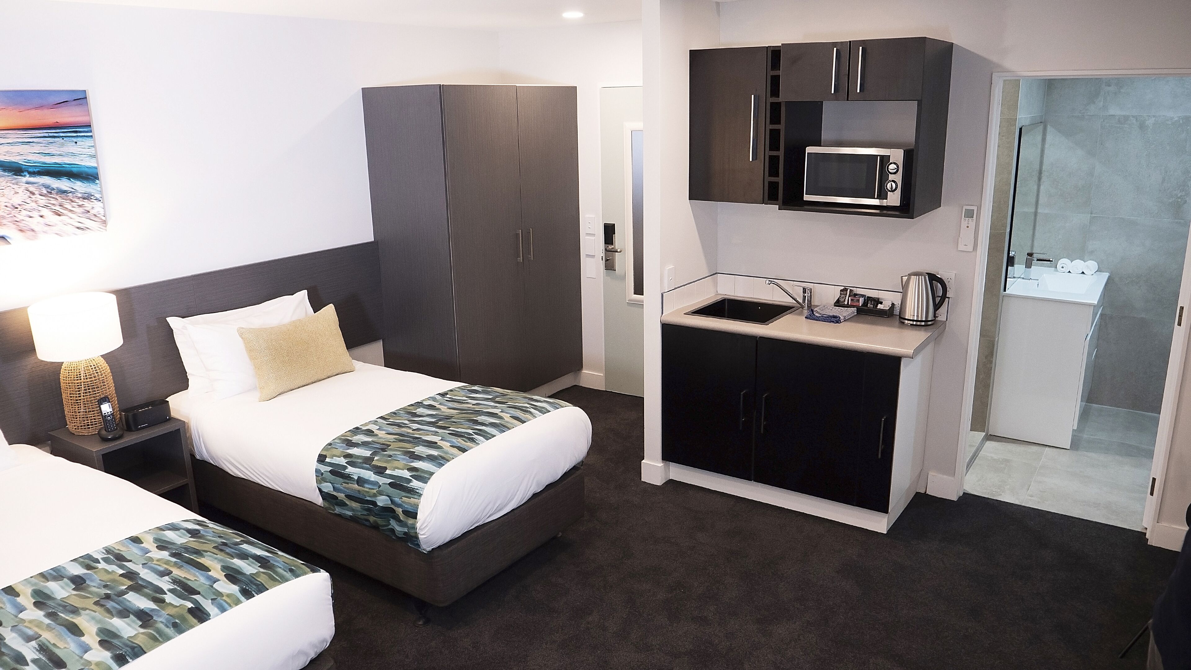 Hotelkamer met een bed, een bureau met lamp, een kitchenette met magnetron en een douche.