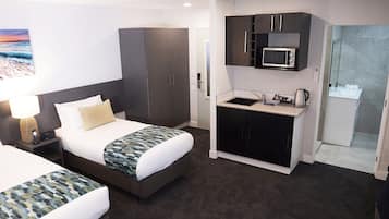 A hotel room with a bed, a desk with a lamp, a kitchenette with a microwave, and a shower area.