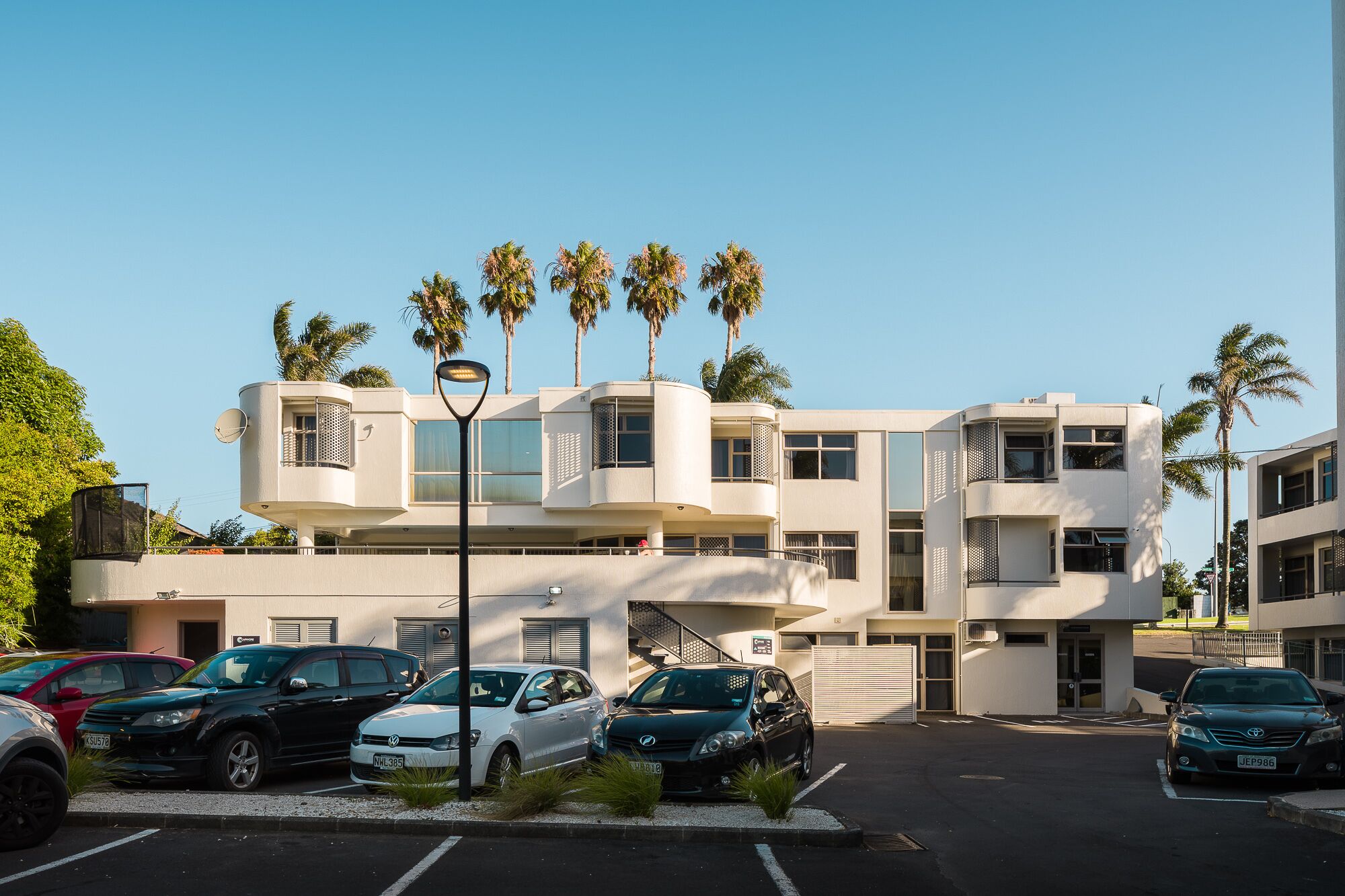 A modern building with a curved facade, multiple balconies, and palm trees.