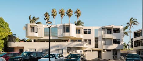 Un bâtiment moderne à la façade incurvée, doté de nombreux balcons et agrémenté de palmiers.