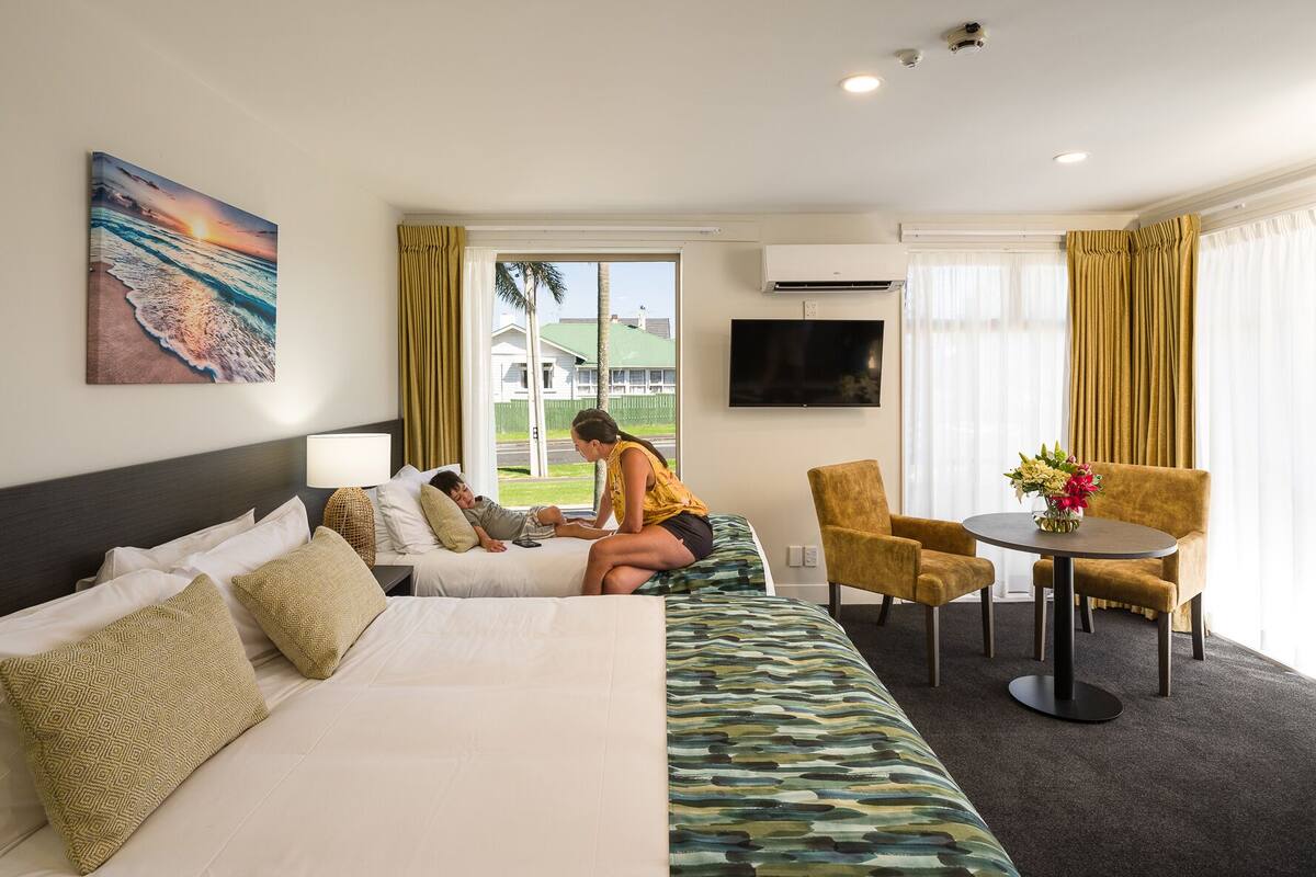 A hotel room with a bed, a sofa, a TV, a table with chairs, and a window with curtains.