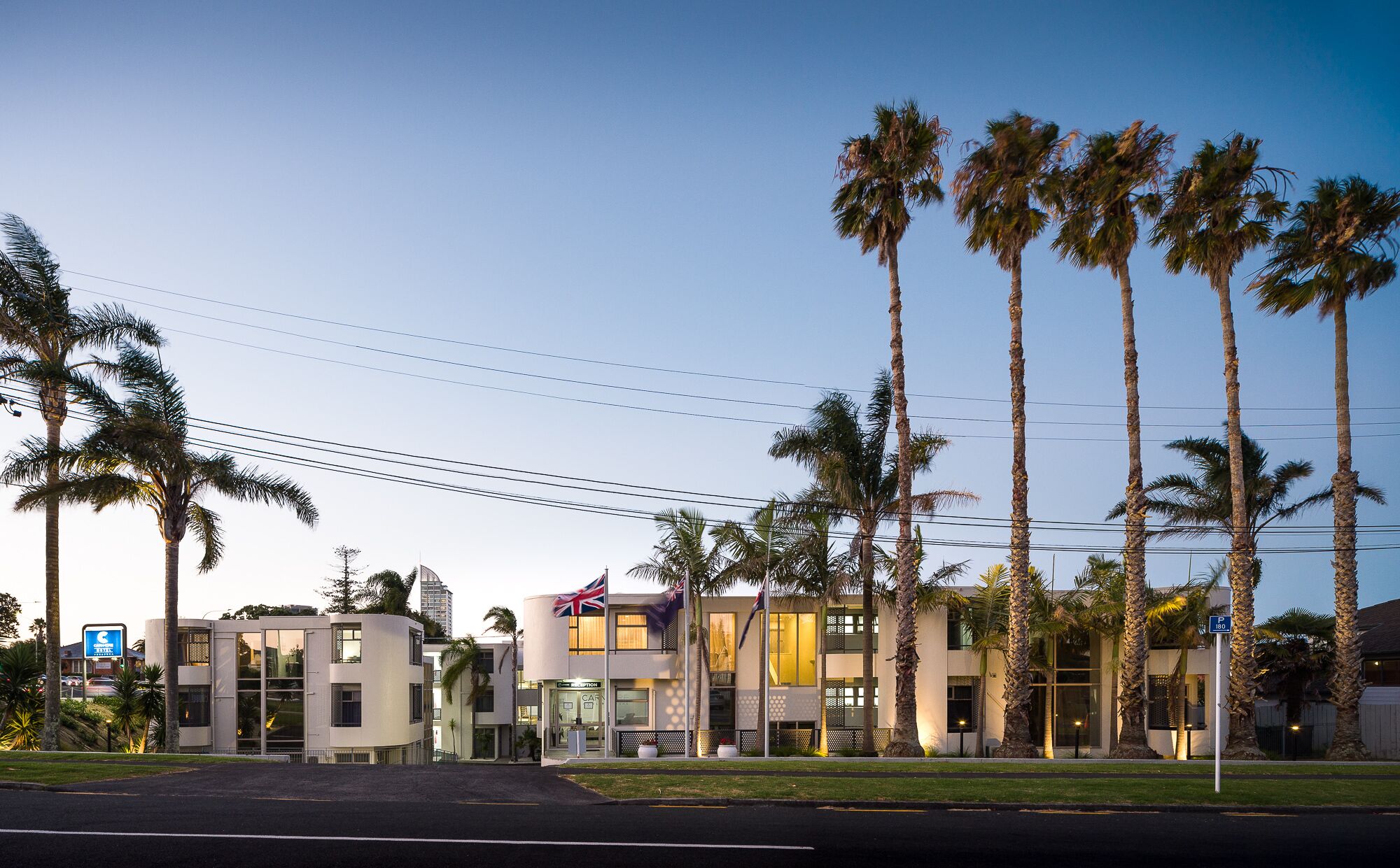 A modern hotel with multiple floors, palm trees, and flags.
