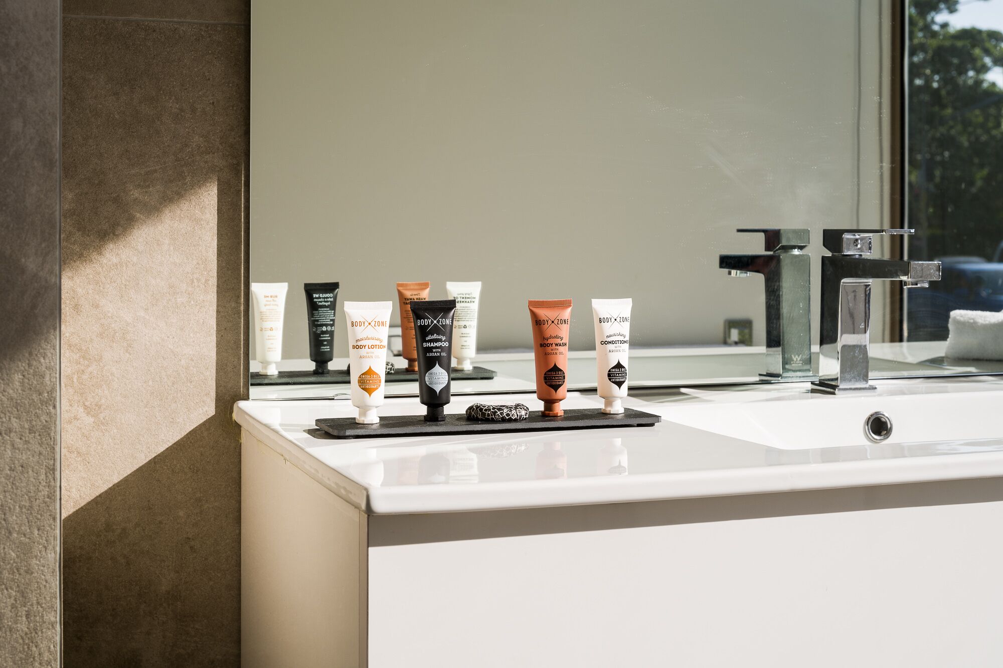 A bathroom with a white sink, a mirror, and various toiletries on a black tray.
