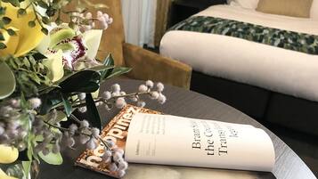 Una habitación de hotel con una cama, una mesita de noche con un libro y un jarrón de flores.