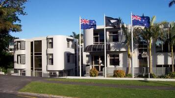 Un edificio moderno con varias banderas, incluyendo las de Australia y Nueva Zelanda, y un césped bien cuidado.