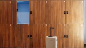 Conjunto de taquillas de madera numeradas del 1 al 10, con una abierta que muestra su interior azul. Una maleta beige está colocada frente a las taquillas.