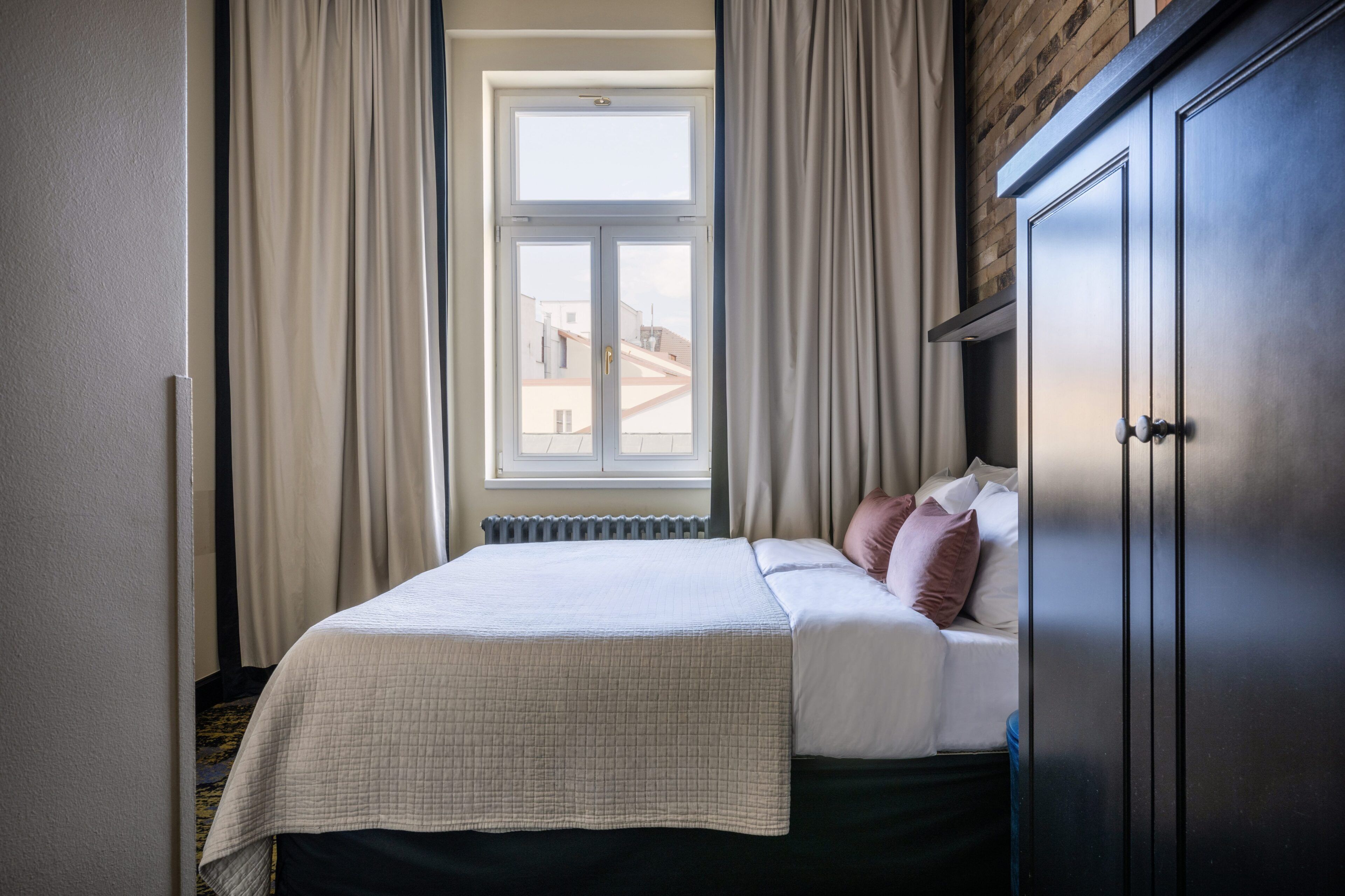 A bedroom with a bed, a radiator, a window with curtains, and a wardrobe.