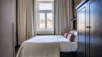 A bedroom with a bed, a radiator, a window with curtains, and a wardrobe.