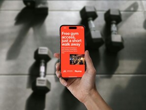 A hand holding a smartphone displaying a message about free gym access at a nearby John Reed Fitness during a Numa stay. - Numa Prague Root (Prague)