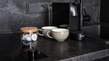 A kitchen counter with a coffee maker, a glass jar with tea bags, and three ceramic cups.