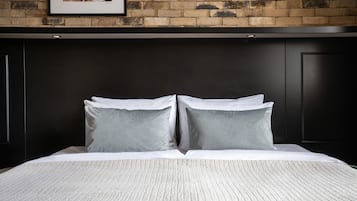 A bed with a white textured bedspread and two pillows, set against a brick wall with a framed picture above.