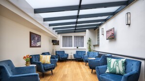 A modern lounge area with blue upholstered chairs, a wooden floor, and a skylight ceiling. - Numa Prague Root (Prague)