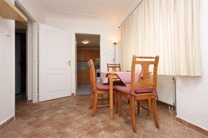 A dining area with a table and four chairs, a white door, a kitchen in the background, and a radiator on the wall. - At the Golden Plough Apartments (Prague)