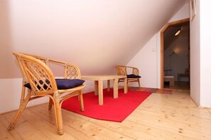 A room with a wooden floor, a red rug, two wicker chairs with cushions, and a wooden table. - At the Golden Plough Apartments (Prague)