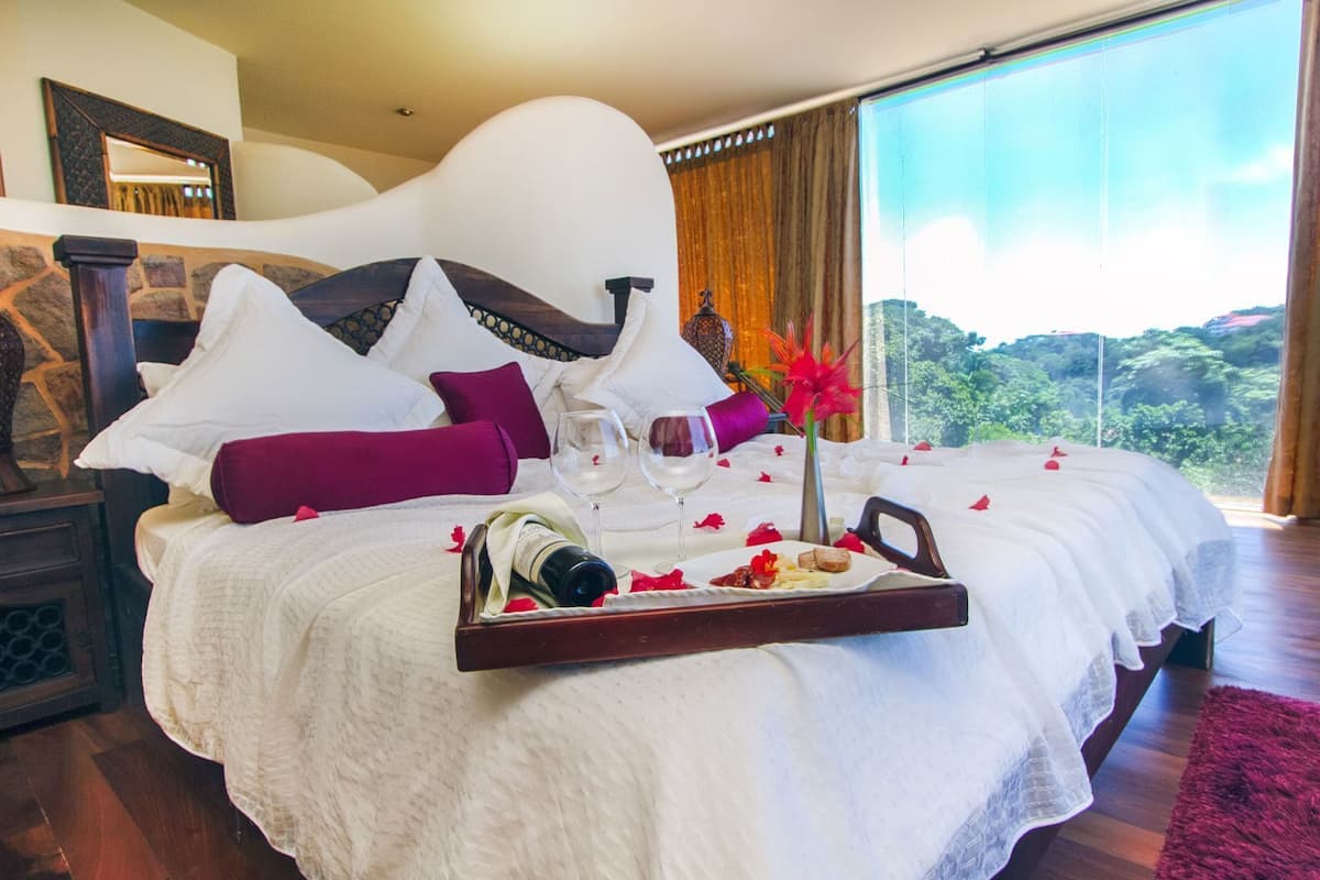 A bedroom with a large bed, a tray with food and drinks, and a view of greenery outside.