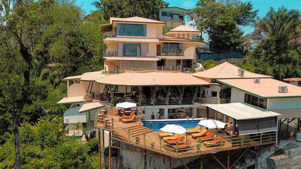 A multi-story building with a pool area on the ground floor, surrounded by lush greenery.
