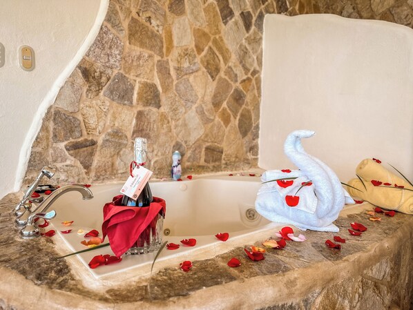 Un baño con suelo de piedra, una bañera, una botella de champán y una toalla con motivos de rosas rojas.