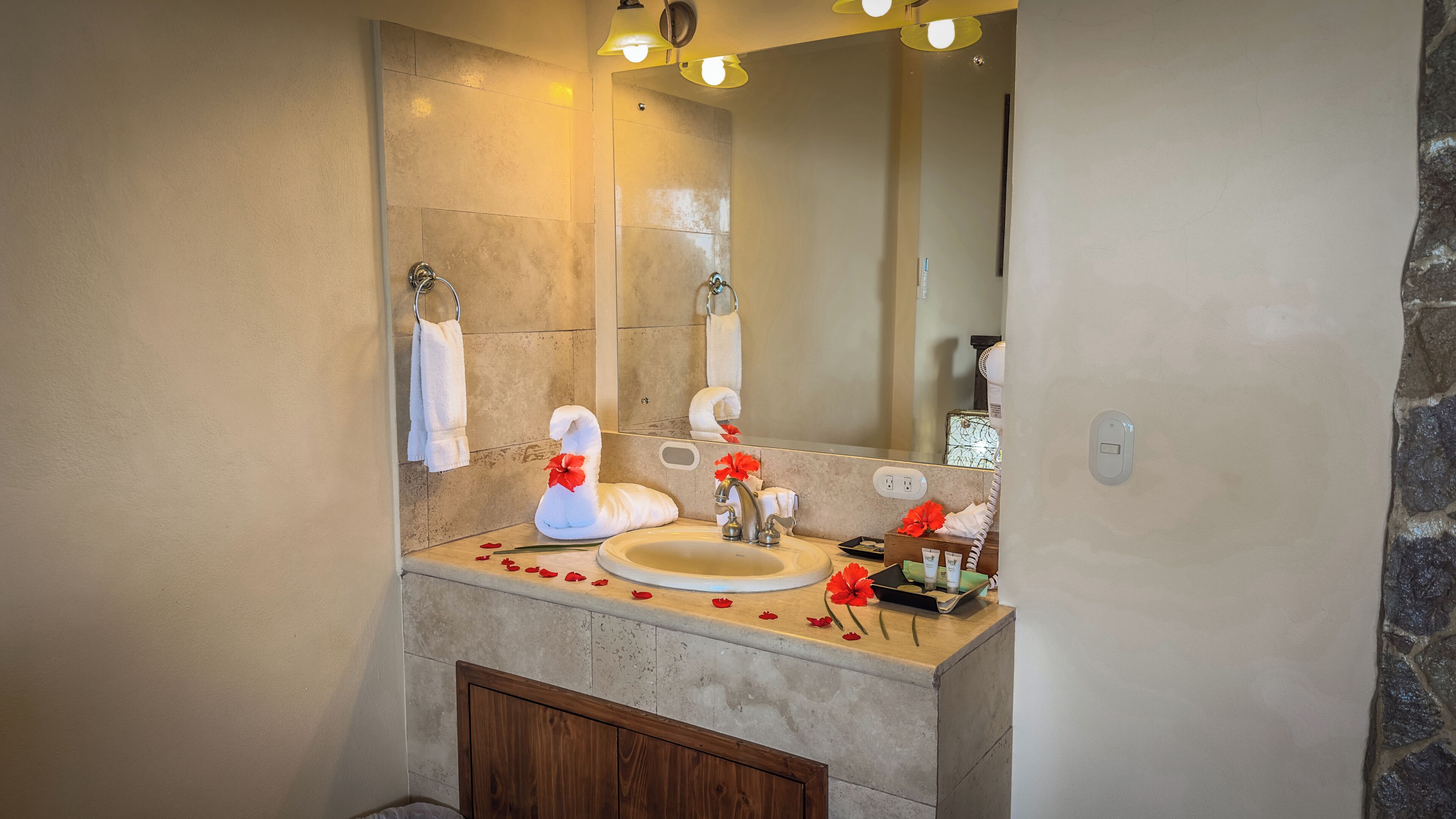 Un baño con pared de baldosas color beige, un armario de madera, un lavamanos con espejo y un perchero con toallas blancas.