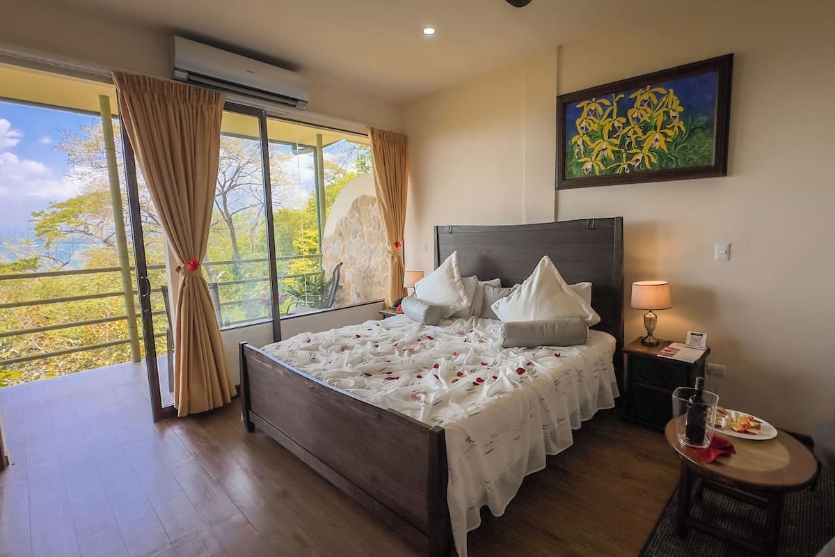A bedroom with a large bed, a nightstand, a table with a drink, and a painting on the wall.