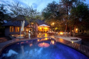 Uma área de piscina com hidromassagem, espreguiçadeiras e um espaço de refeições com mesa e cadeiras.