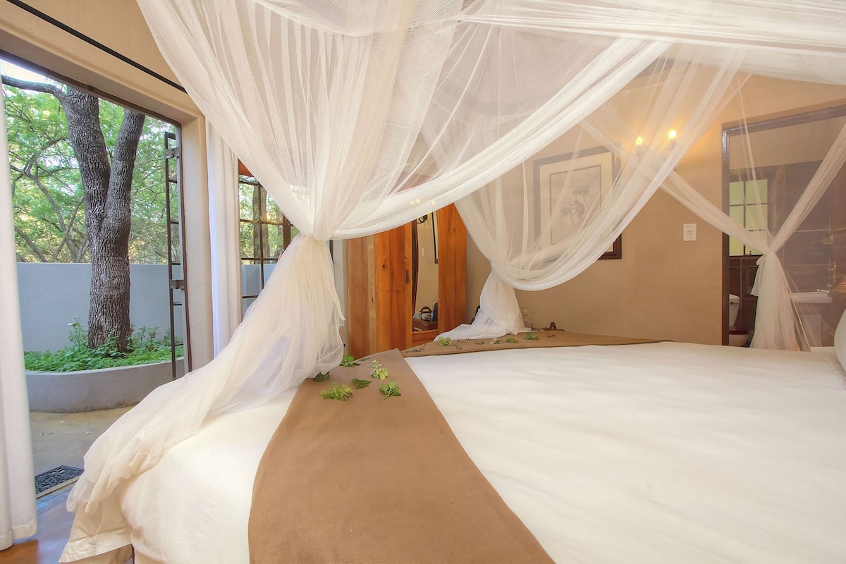 A bedroom with a large bed, white curtains, and a view of trees outside.