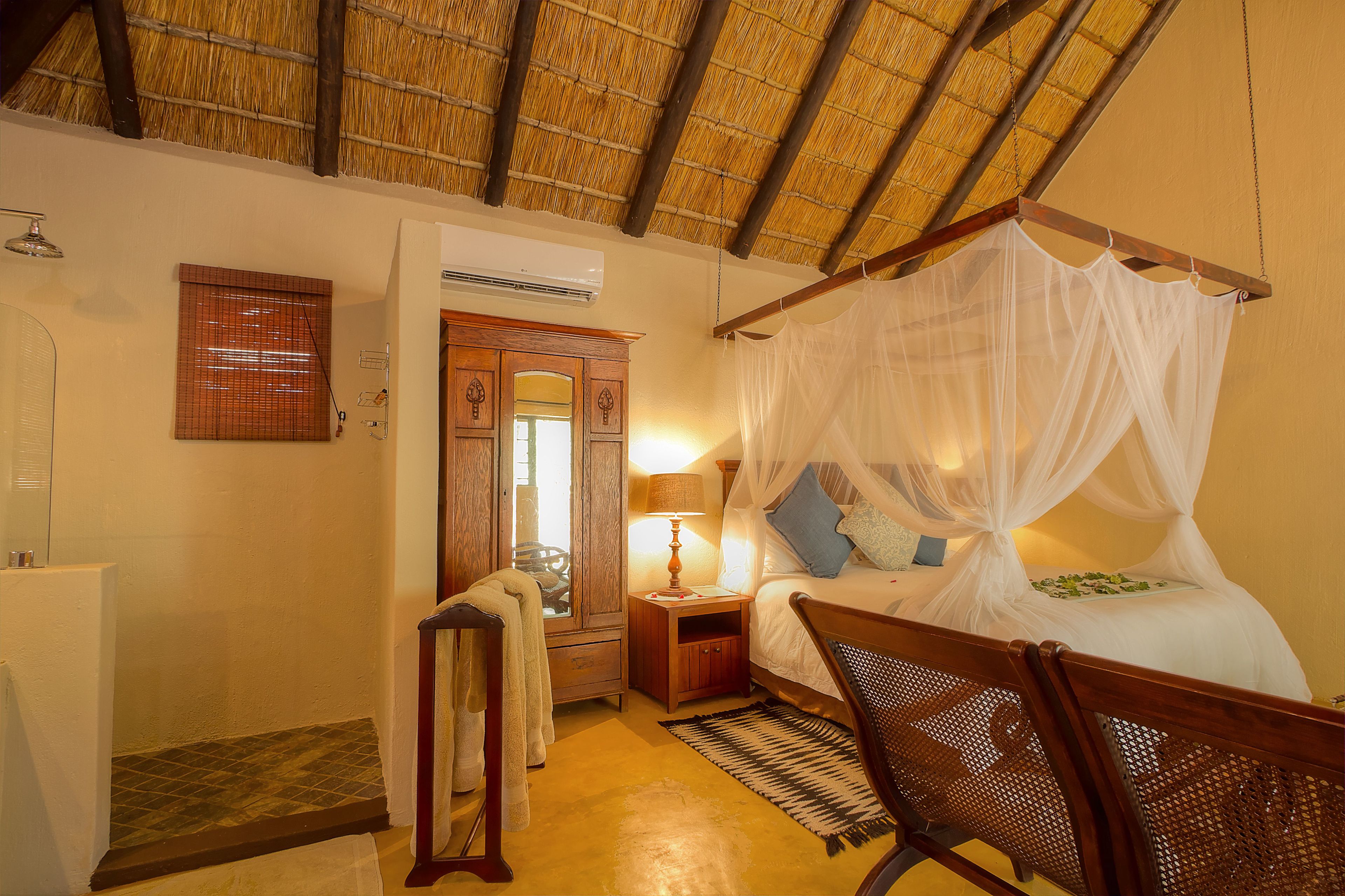 A bedroom with a canopy bed, a wooden nightstand, a lamp, a mirror, and a shower area.