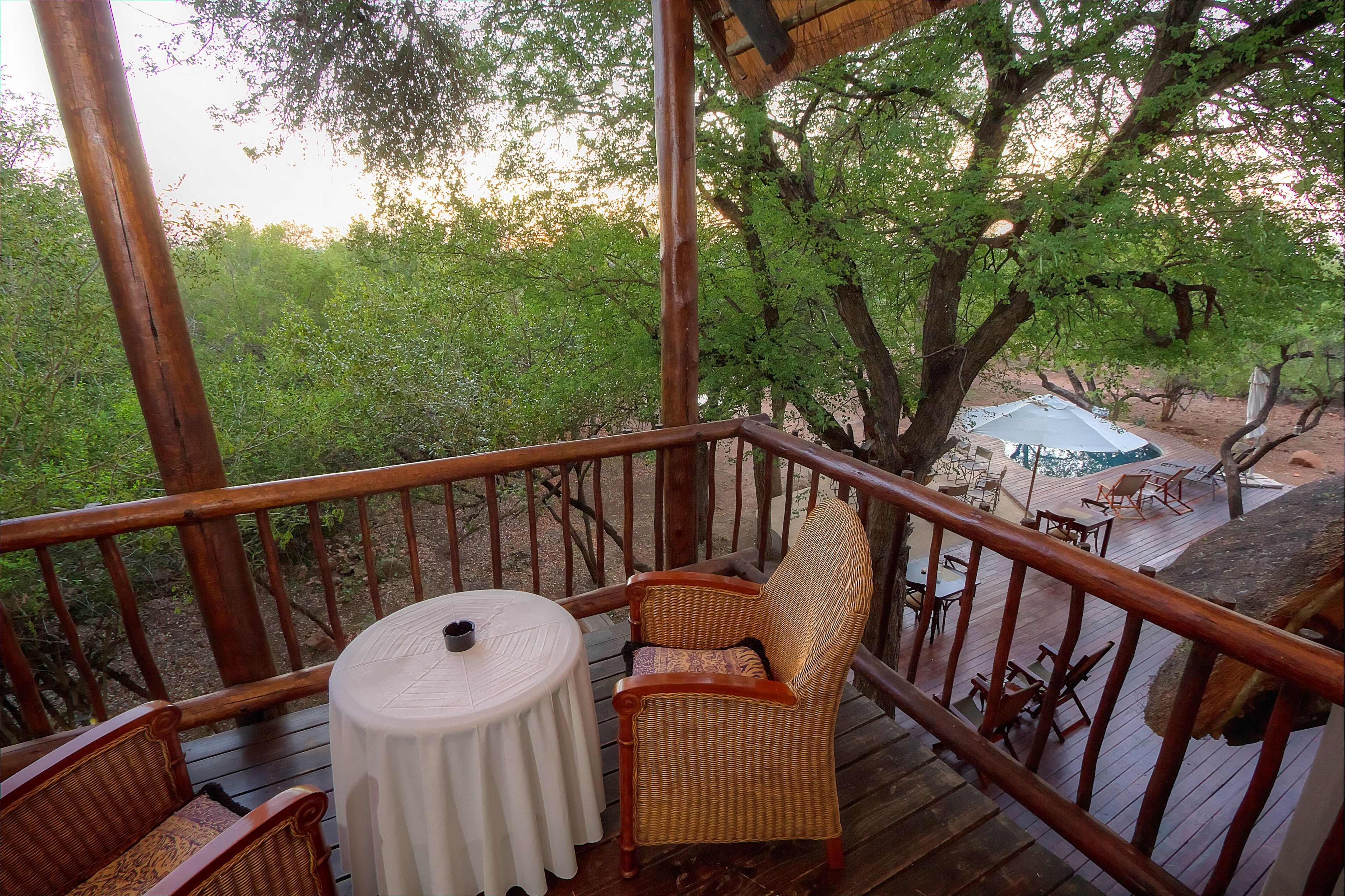 A wooden deck with wicker furniture, a round table, and a view of a wooded area.