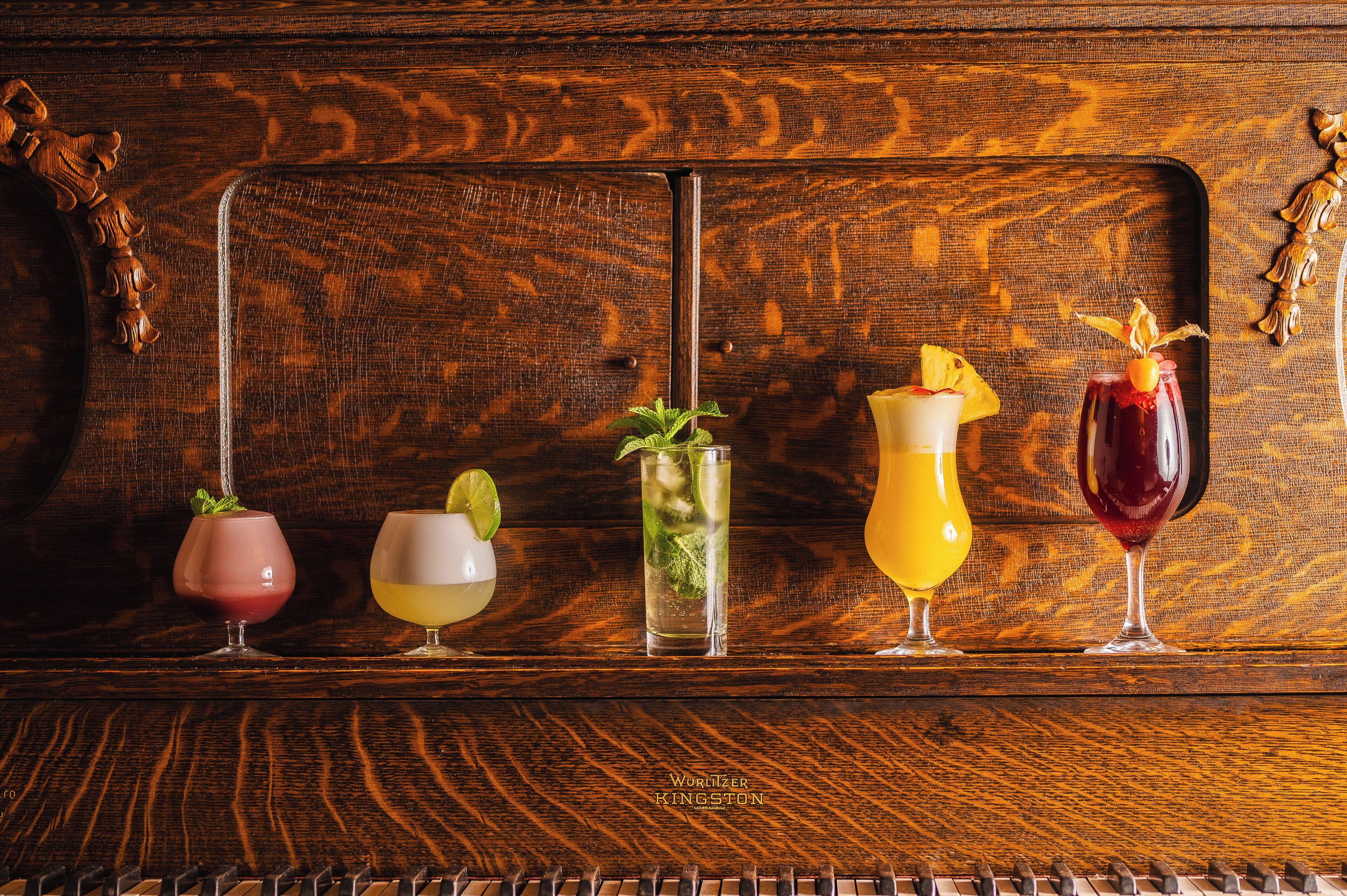 Una barra de madera con cinco vasos de diferentes bebidas.