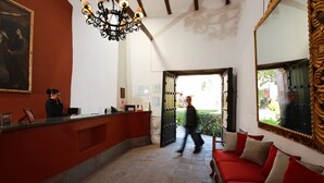 Un área de recepción con un mostrador para recepcionista, una araña de cristal, un sofá rojo y un espejo grande.