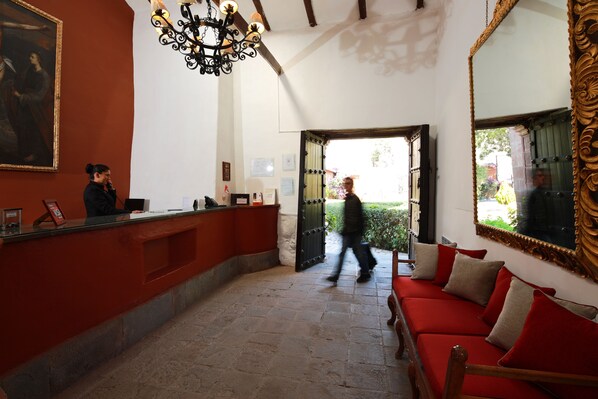 A reception area with a receptionist desk, a chandelier, a red sofa, and a large mirror. - Boutique San Agustín Monasterio de la Recoleta (Urubamba)