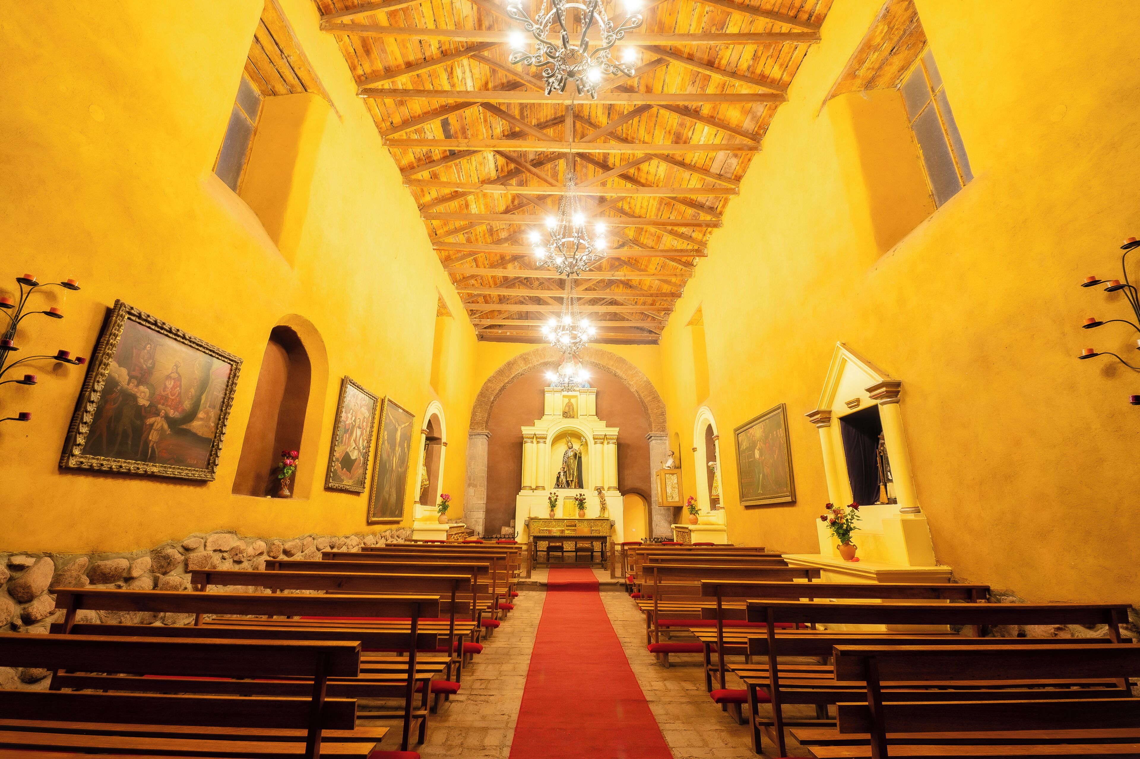 Interior de una iglesia con bancas de madera, un pasillo con alfombra roja y un altar central.