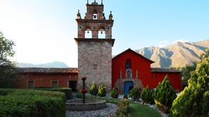Un edificio histórico con una torre de campanas, fachada roja y un camino de piedra que lleva a una fuente.