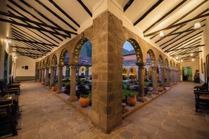 Un patio con columnas de piedra, arcos y plantas en macetas.