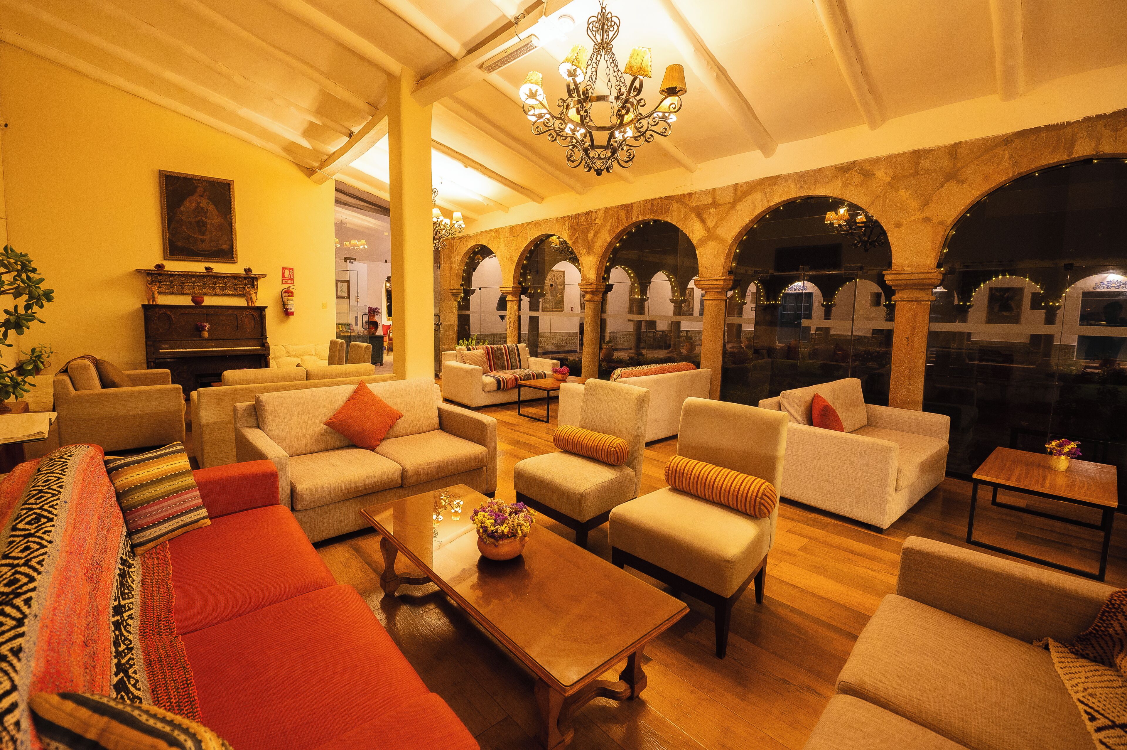 A spacious lobby with multiple seating areas, a grand chandelier, and a view through an arched doorway.