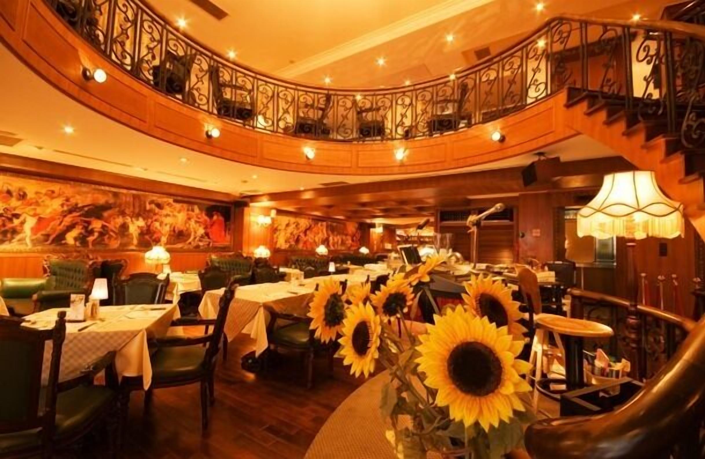 A restaurant with round tables, sunflowers, and a curved staircase.