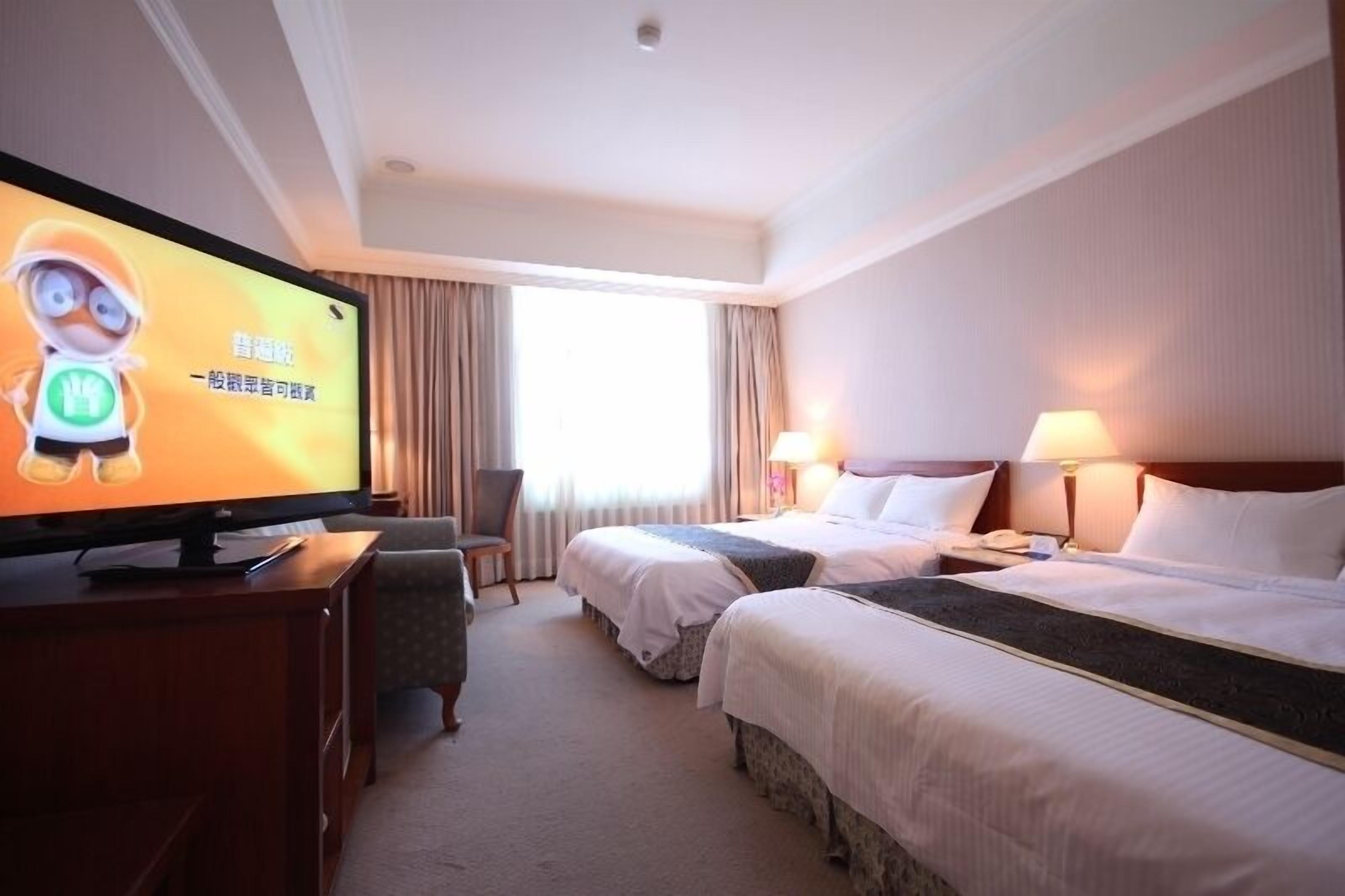 A hotel room with two beds, a TV, a desk, and a chair.