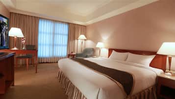 A hotel room with a large bed, a desk with a chair, a television, and two lamps.
