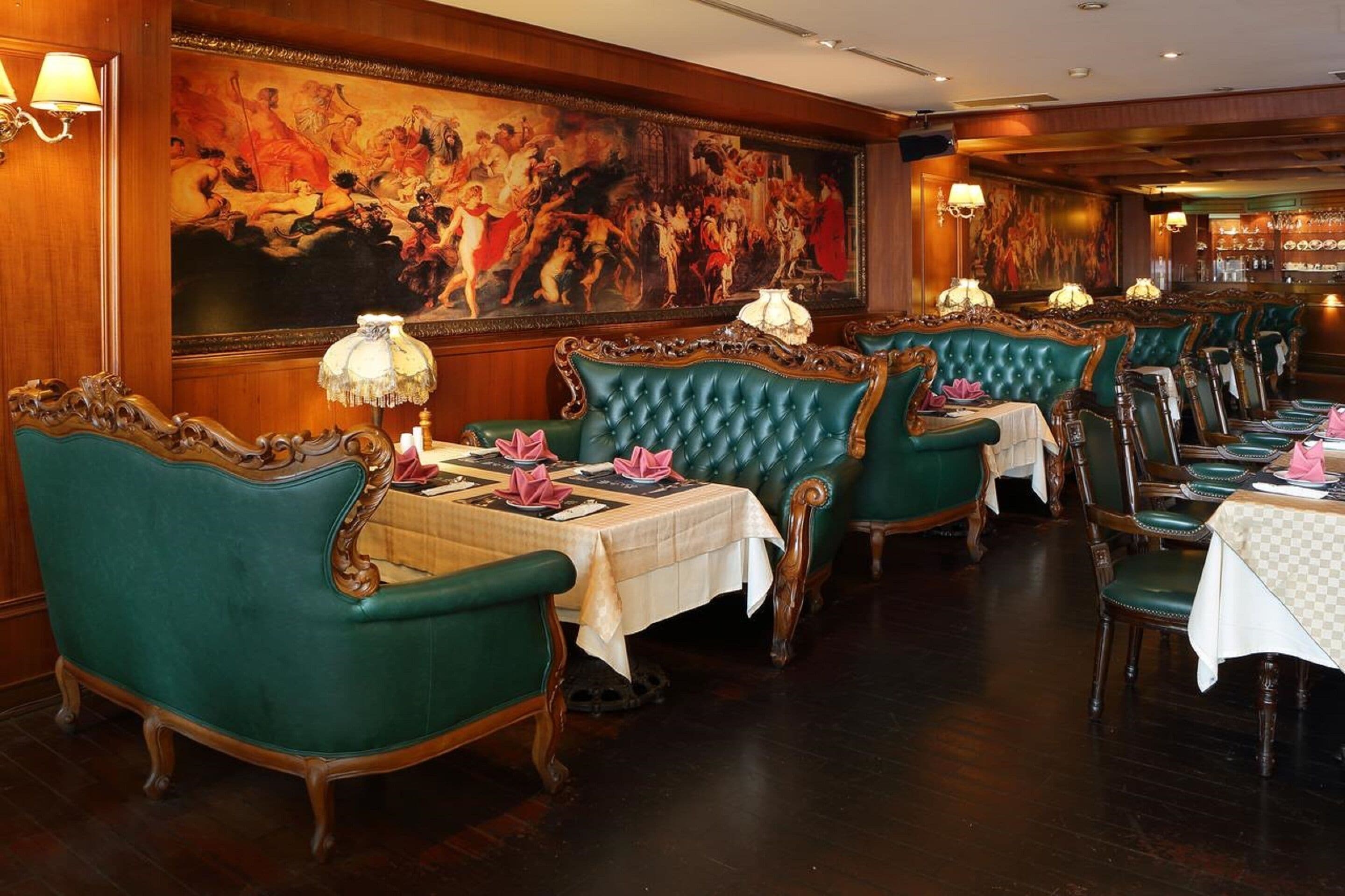 Un ristorante con sedie rivestite di verde, tovaglie bianche e un grande dipinto classico appeso al muro.